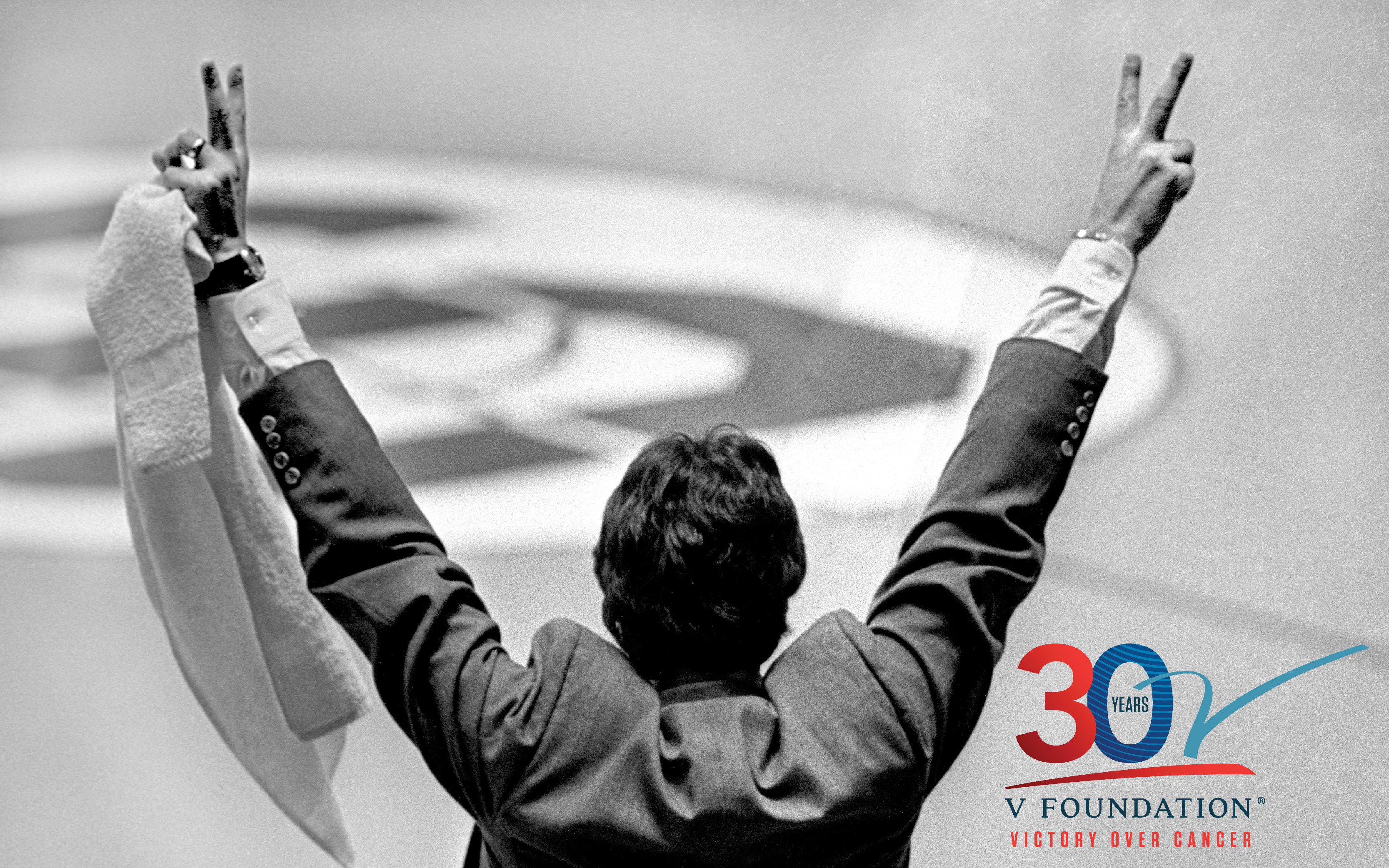 Photo of Jim Valvano from the back holding both hands high with his fingers in a "V" for Victory, and the V Foundation 30th Anniversary logo